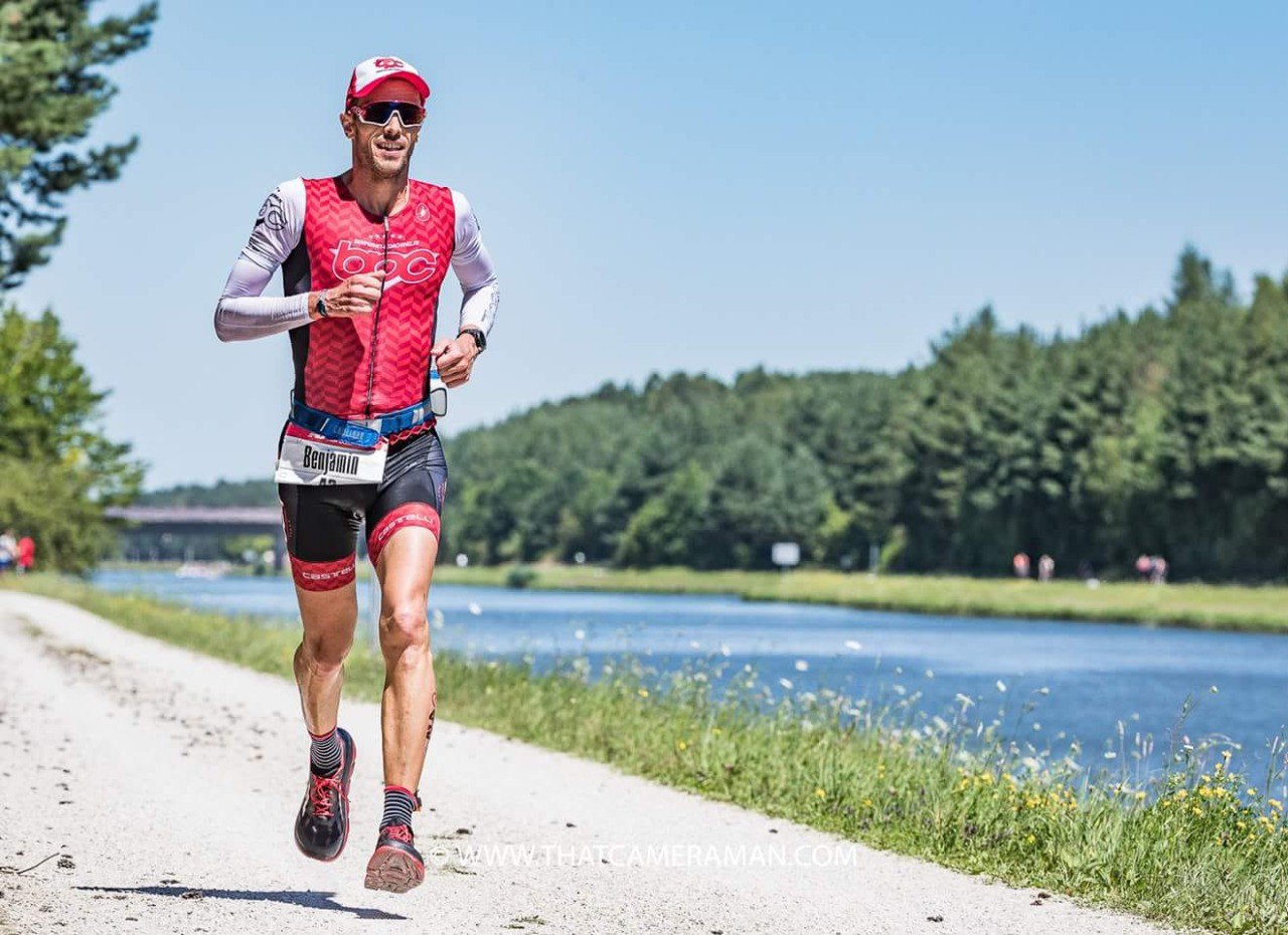 Benjamin Pernet en course à pied sur un triathlon, trisuit BPC rouge, au bord de l'eau